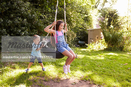 Brother Pushing Sister On Tire Swing In Garden