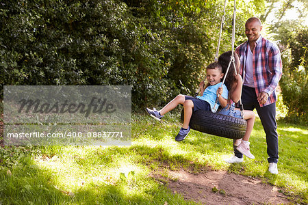 Father Pushing Children On Tire Swing In Garden