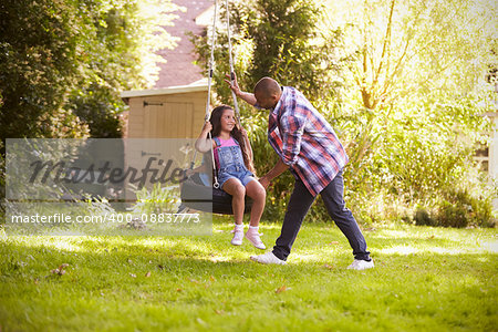 Father Pushing Daughter On Tire Swing In Garden