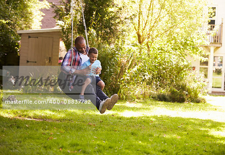 Father And Son Having Fun On Tire Swing In Garden