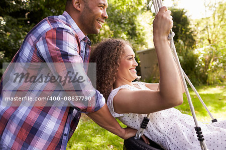 Side View Of Man Pushing Woman On Tire Swing In Garden