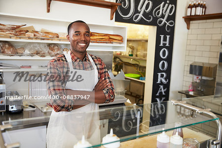 Owner behind the counter of sandwich bar with arms crossed