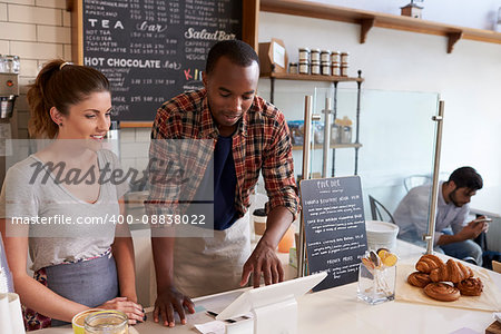 Barista at coffee shop showing till to new employee, close up