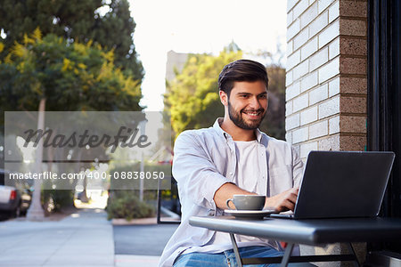 Bearded young man using a laptop at a table outside a cafe