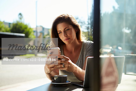 Young white woman using smartphone at a table outside a cafe