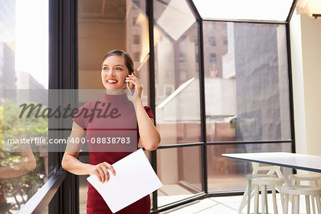 Smiling young white businesswoman on phone in modern office