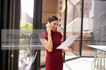 Smiling white woman on phone in office looking at document