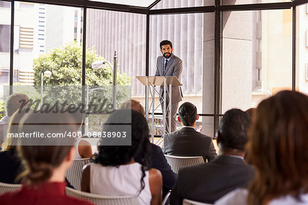 Hispanic man presenting business seminar leaning on lectern