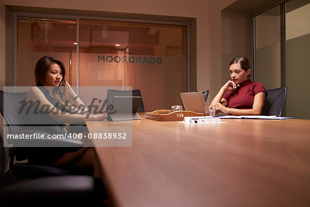 Two businesswomen working late in office using computers