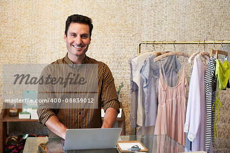 Young man working in clothes shop using laptop at counter