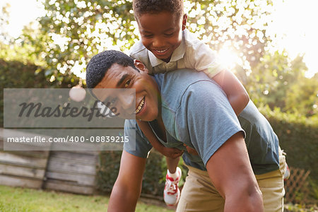 Young black boy playing on dadÕs back in a garden, low angle