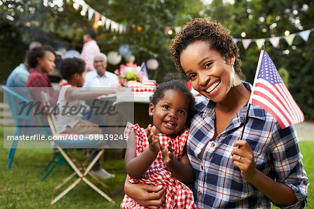 Black mother and baby hold flag at 4th July party, to camera