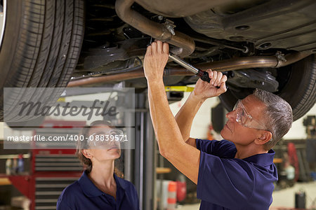 Male And Female Mechanics Working Underneath Car Together