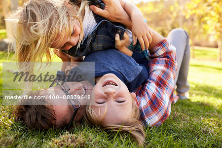 Two young kids lying on top of their dad in a park