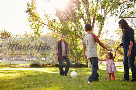 Young mixed race family playing with ball in a park, backlit