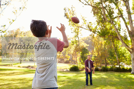 Dad and son throwing American football to each other in park