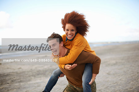 Couple playing piggyback on beach