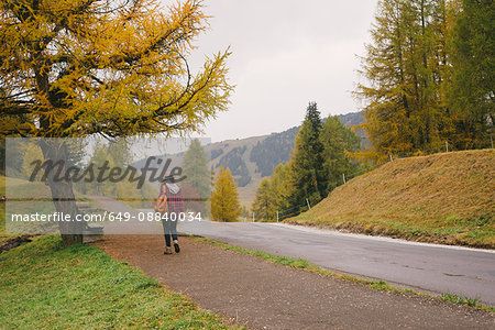 Hiker walking by road, Alpe di Siusi park, Dolomite Alps, South Tyrol, Italy