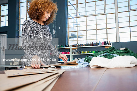 Mature female fashion designer preparing pattern on workshop table