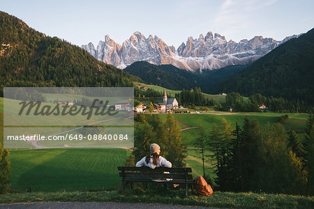 Woman relaxing on park bench, Santa Maddalena, Dolomite Alps, Val di Funes (Funes Valley), South Tyrol, Italy