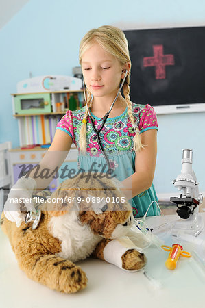 Girl pretending to be vet examining toy tiger using stethoscope