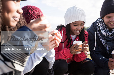 Young adult friends crouching on beach with coffee takeaway, Western Cape, South Africa