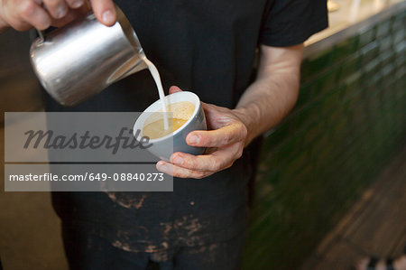 Male barista's hands pouring milk into coffee cup in cafe