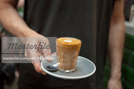 Cropped shot of barista holding glass of coffee in cafe