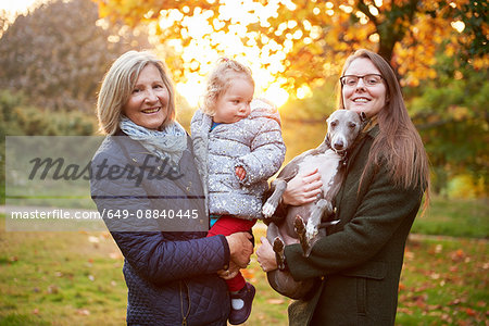 Portrait of senior woman with daughter, granddaughter and dog in autumn park