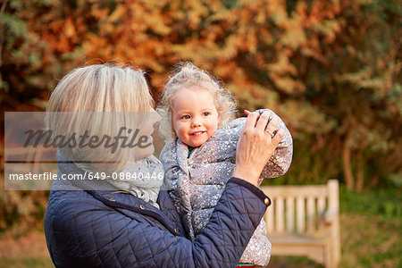 Senior woman carrying toddler granddaughter in autumn park