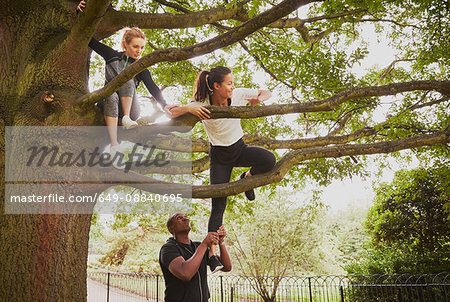 Personal trainer giving woman helping hand to climb park tree