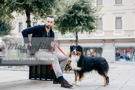 Man with dog smoking cigarette on city street bench