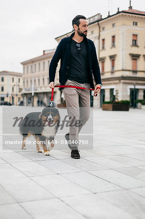 Mid adult man walking dog at city square