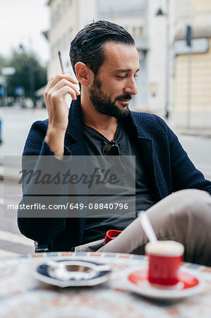 Mid adult man smoking cigarette at sidewalk cafe