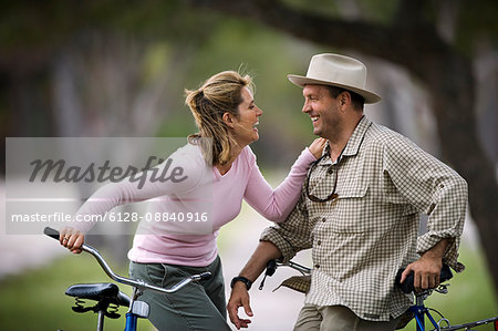 Mid-adult couple laughing with each other as they lean on bicycles.