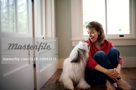 Middle-aged woman sits on the floor of her living room and smiles and talks with her dog.
