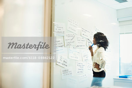 A woman standing in an office looking at pieces of paper pinned on a whiteboard.