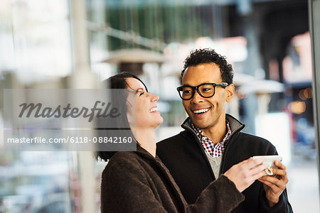 A young man and woman holding a cellphone together and laughing.