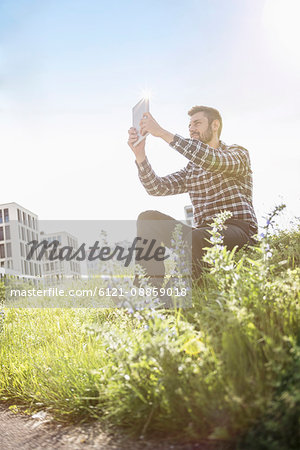 Young man taking self portrait photography with digital tablet in the park, Munich, Bavaria, Germany