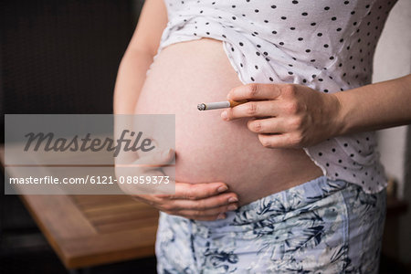 Mid section of pregnant woman holding cigarette in front of her belly, Munich, Bavaria, Germany Mid section of pregnant woman holding cigarette in front of her belly, Munich, Bavaria, Germany