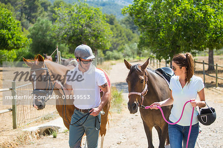 Male and female grooms leading horses from paddock at rural stables