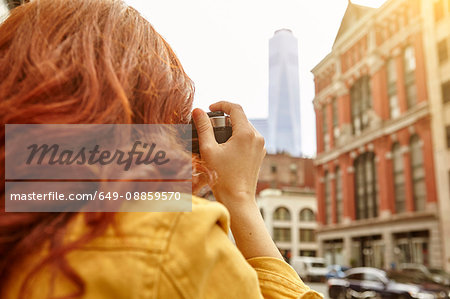 Young female tourist with long red hair photographing One World Trade Centre, Manhattan, New York, USA