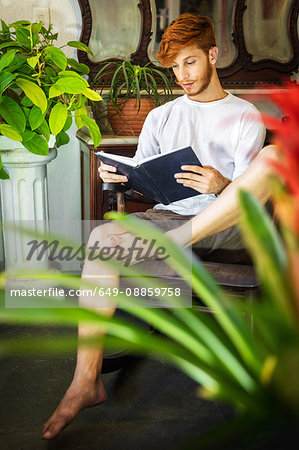 Young man with red hair, sitting in chair, reading book