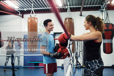 Female boxer leaning on boxing ring ropes talking to male boxer
