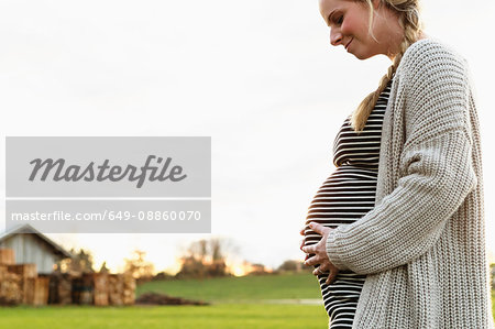 Pregnant mid adult woman holding stomach with head down in field landscape