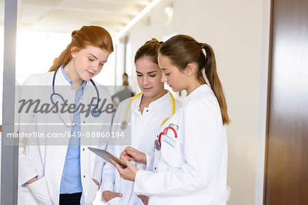 Three young female doctors looking at digital tablet in hospital corridor