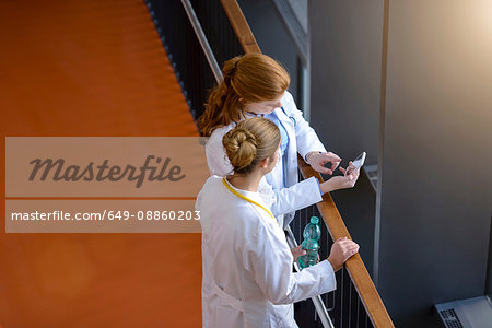 High angle view of two female doctors on hospital balcony looking at smartphone