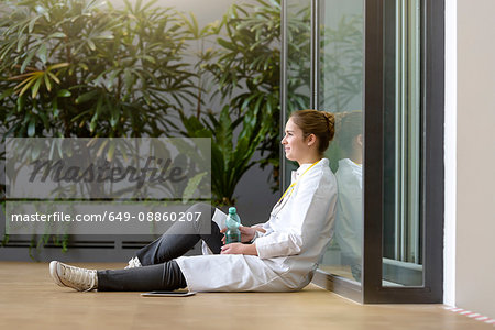 Young female doctor sitting on floor at hospital entrance