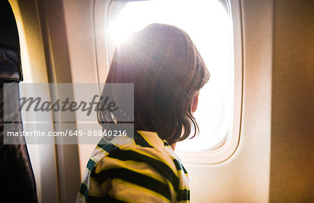 Boy on airplane looking through sunlit airplane window