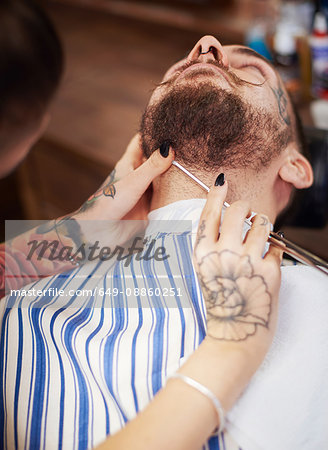 Hairdresser shaving customer's beard